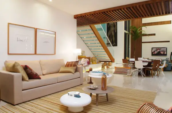 Elegantes salones marrones y beige con sofá, mesas auxiliares, alfombra a rayas y una escalera moderna.